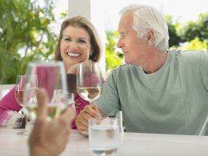 Happy middle aged couple having wine with friend at verandah tab